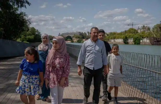 A family of six walking down a boardwalk next to a body of water.