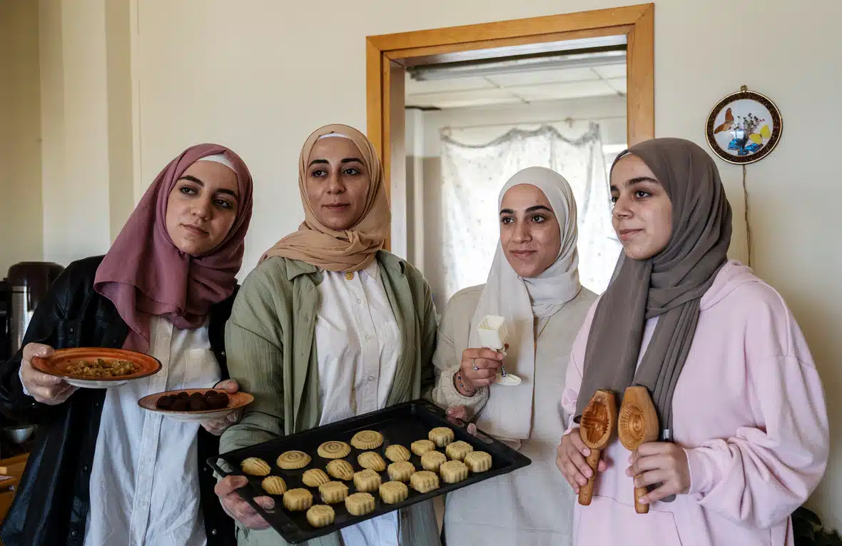 Four women stand in a row holding baking tools and baked goods.