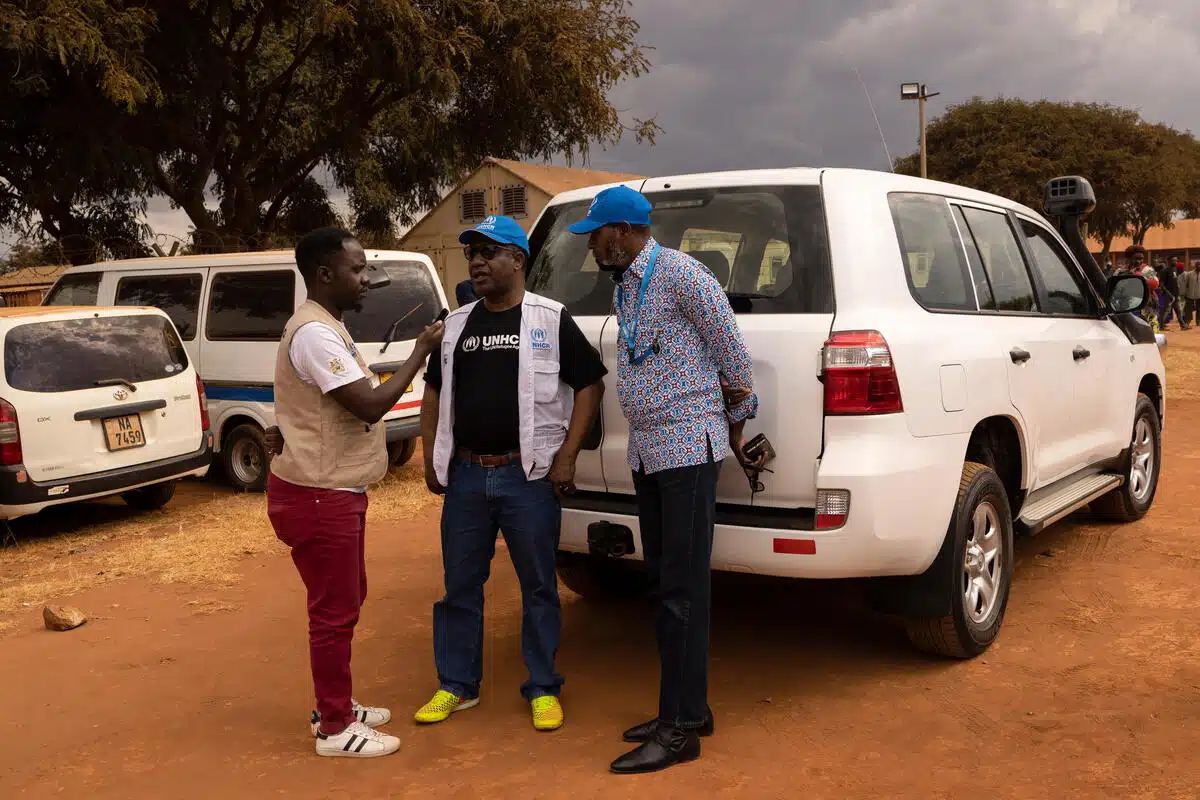 three men stand talking outside a white van in a desert-looking area