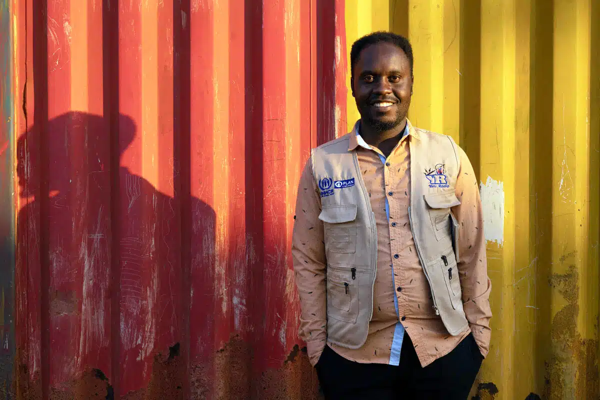 A man stands smiking in front of a wall painted half red half yellow