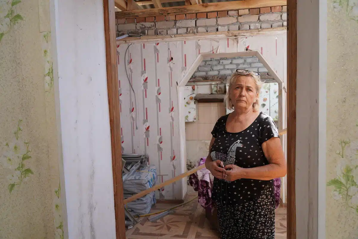 Une femme regarde tristement la caméra alors qu'elle se trouve dans une pièce d'une maison en construction. 