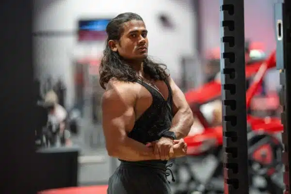 a muscular man with shoulder-length hair flexes in a gym