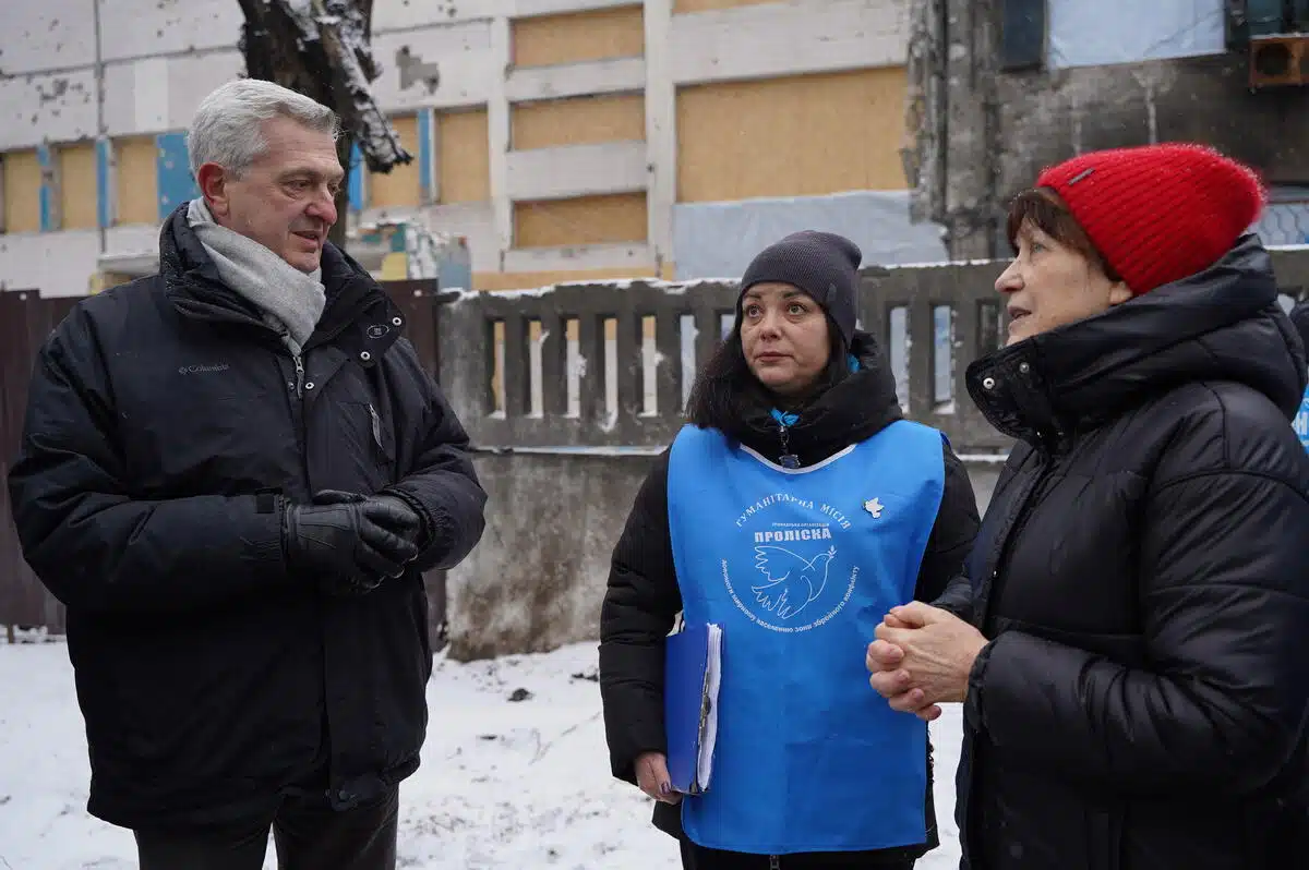 A man with grey hair (Philippo grande) stands next to a woman looking off in the distance tp the left side of the screen