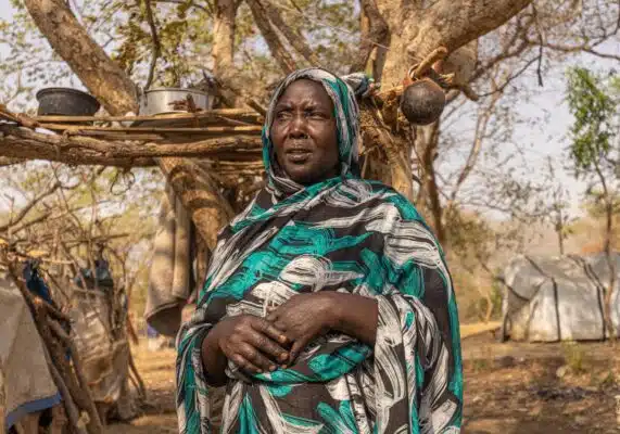 A woman stands in front of a tree with her hands lightly clasped.