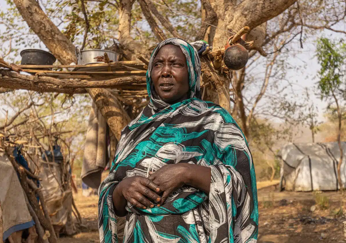 A woman stands in front of a tree with her hands lightly clasped. 