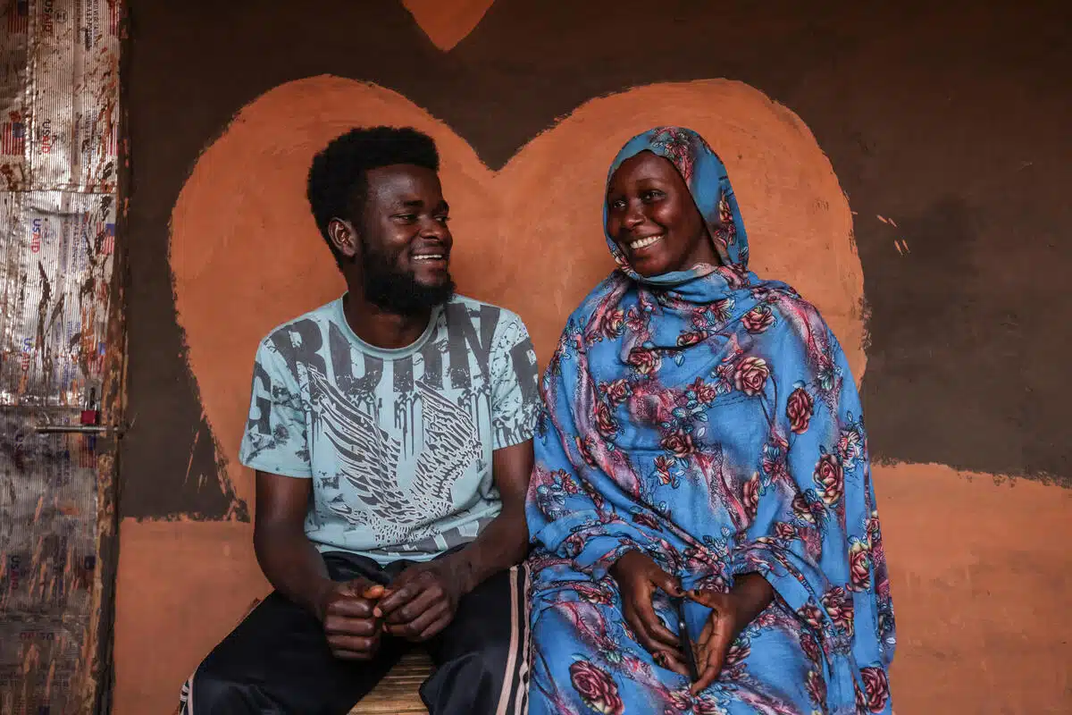 Un homme et une femme se sourient l'un à l'autre alors qu'ils sont assis devant une peinture murale en forme de cœur.