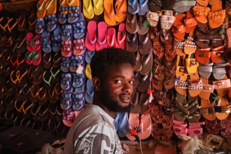 A close-up of a man standing in front of rows of flip-flops on a wall.