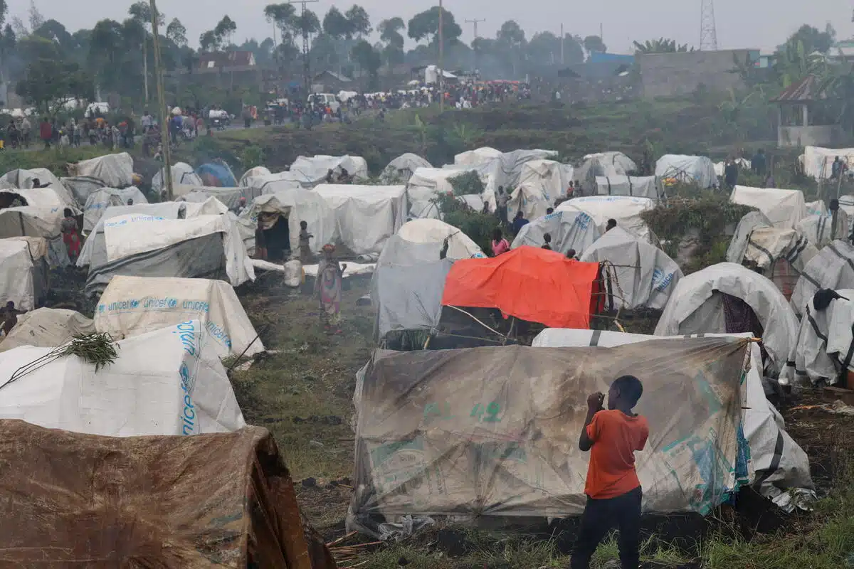 A boy stands facing a camp of makeshift tents made from tarps. 