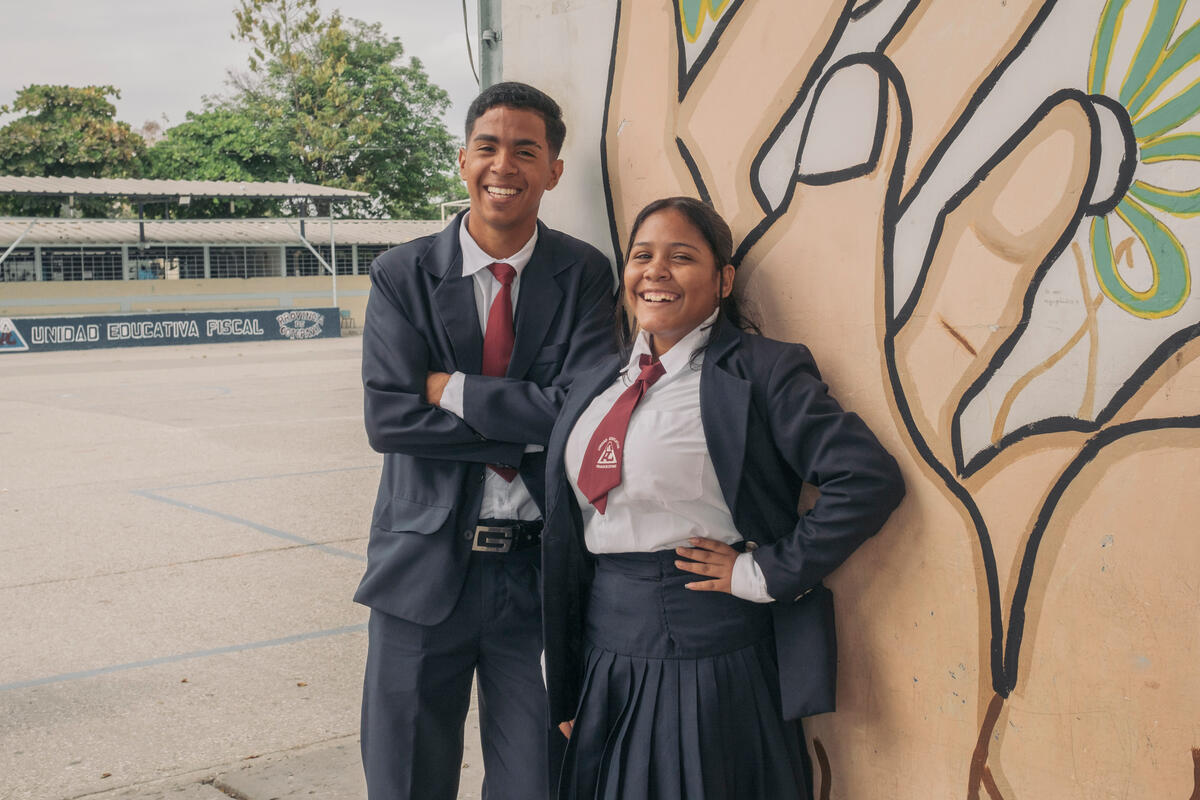 a girl and a boy stand smiling in front of a mural