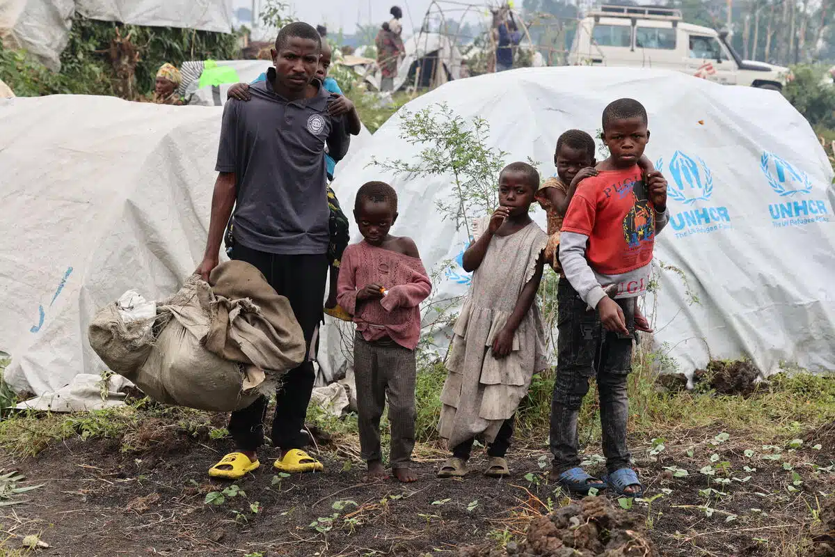 A man walks with children around him, one on his back. 