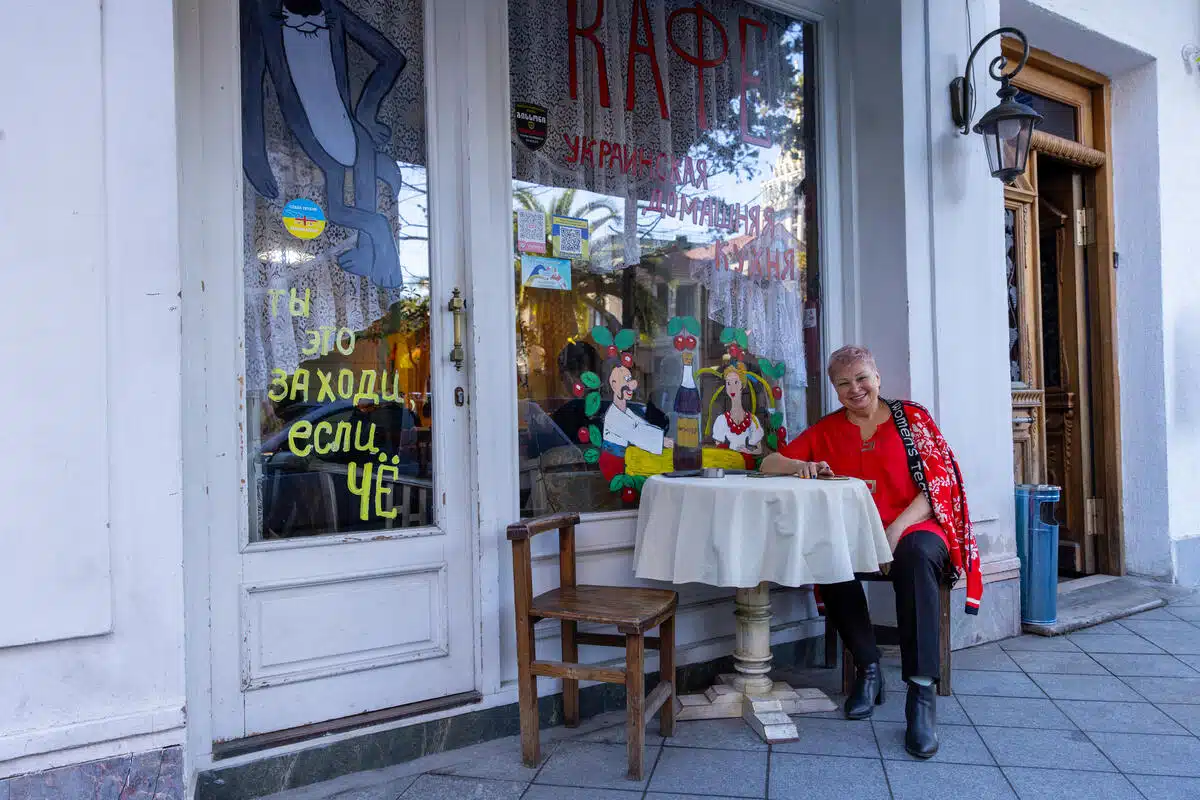Women sits similing at a table in front of a storefront