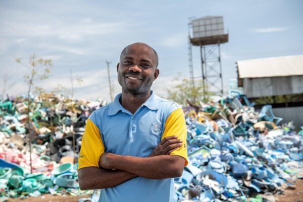 Man in blue shirt and yellow sleeves stands in front of a pile of plastic