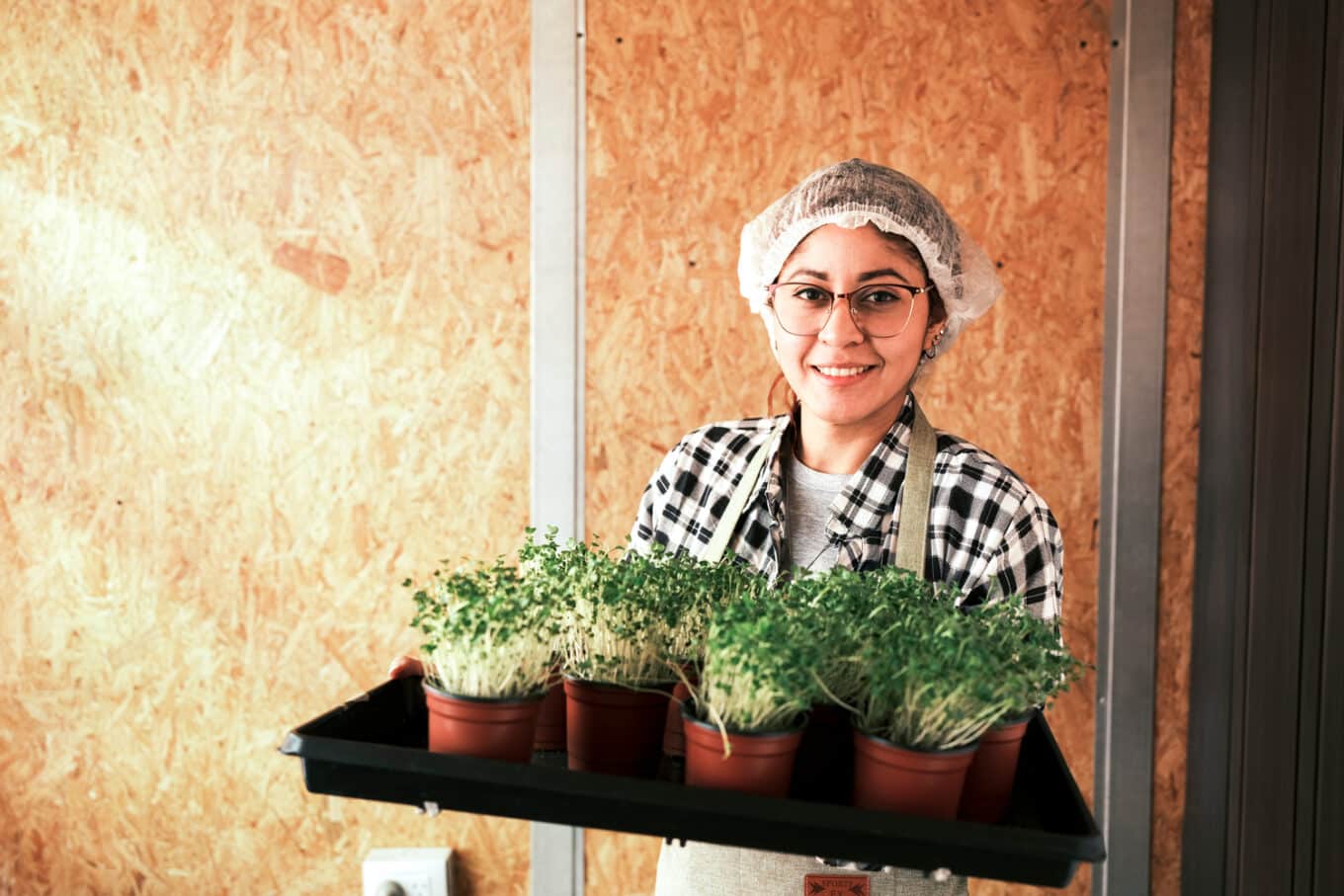 A woman smiles as she hoolds a pamn of potted sprouts 
