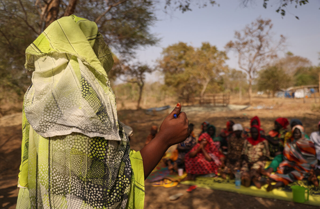 A woman stands in front of a group of people sitting on the ground