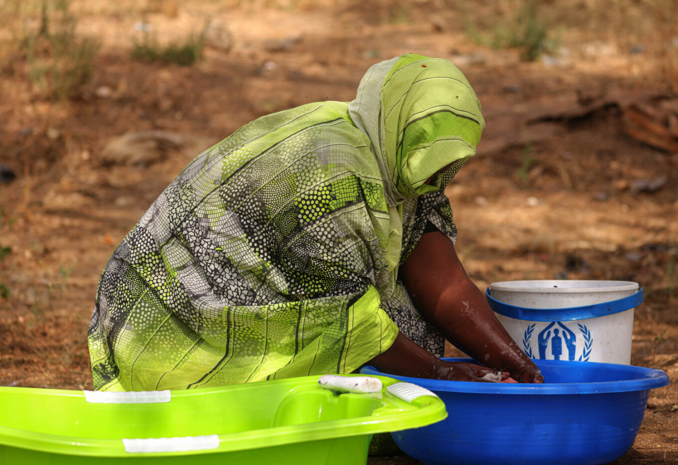 A woman kneels down with her hands in a bucket