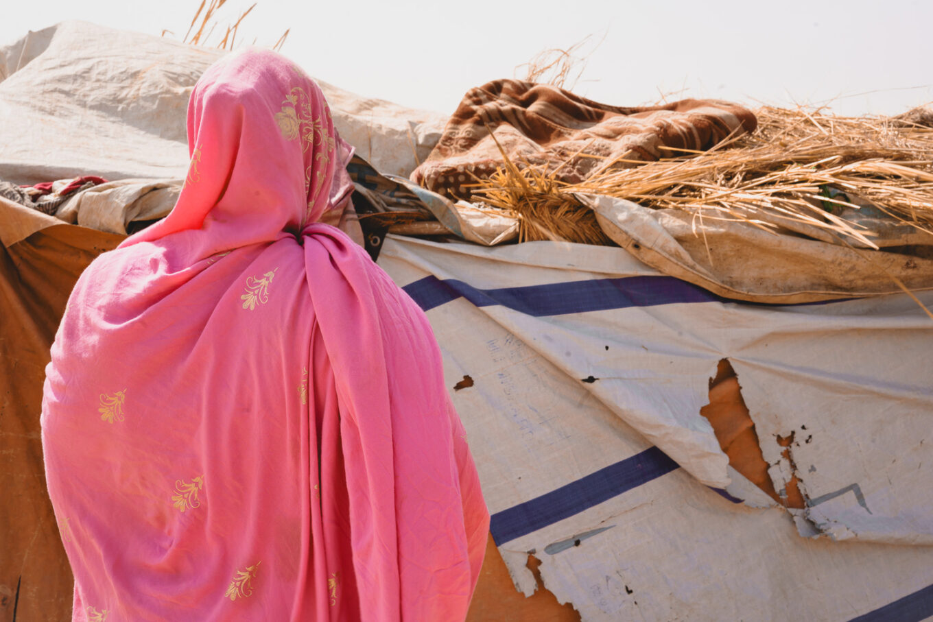 A woman stands with her back turned to the camera in front of a makeshift shelter 