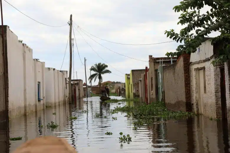 Flooded residential street. There is a person on the boat paddling down the street.