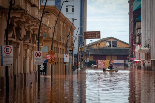 Dirty brown flood water covers a street up to street signs as three rescue workers - two standing chest-deep in the water and the third sitting in a small inflatable boat - navigate floodwaters in the historic city centre of Porto Alegre in the southern Brazilian state of Rio Grande do Sul.