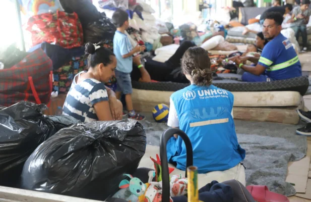 Person with UNHCR-labeled vest sitting with people surrounded by filled plastic bags.