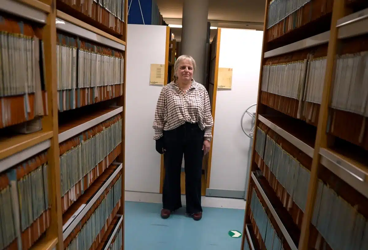 There is a woman standing alone in a hallway in between bookshelves. 