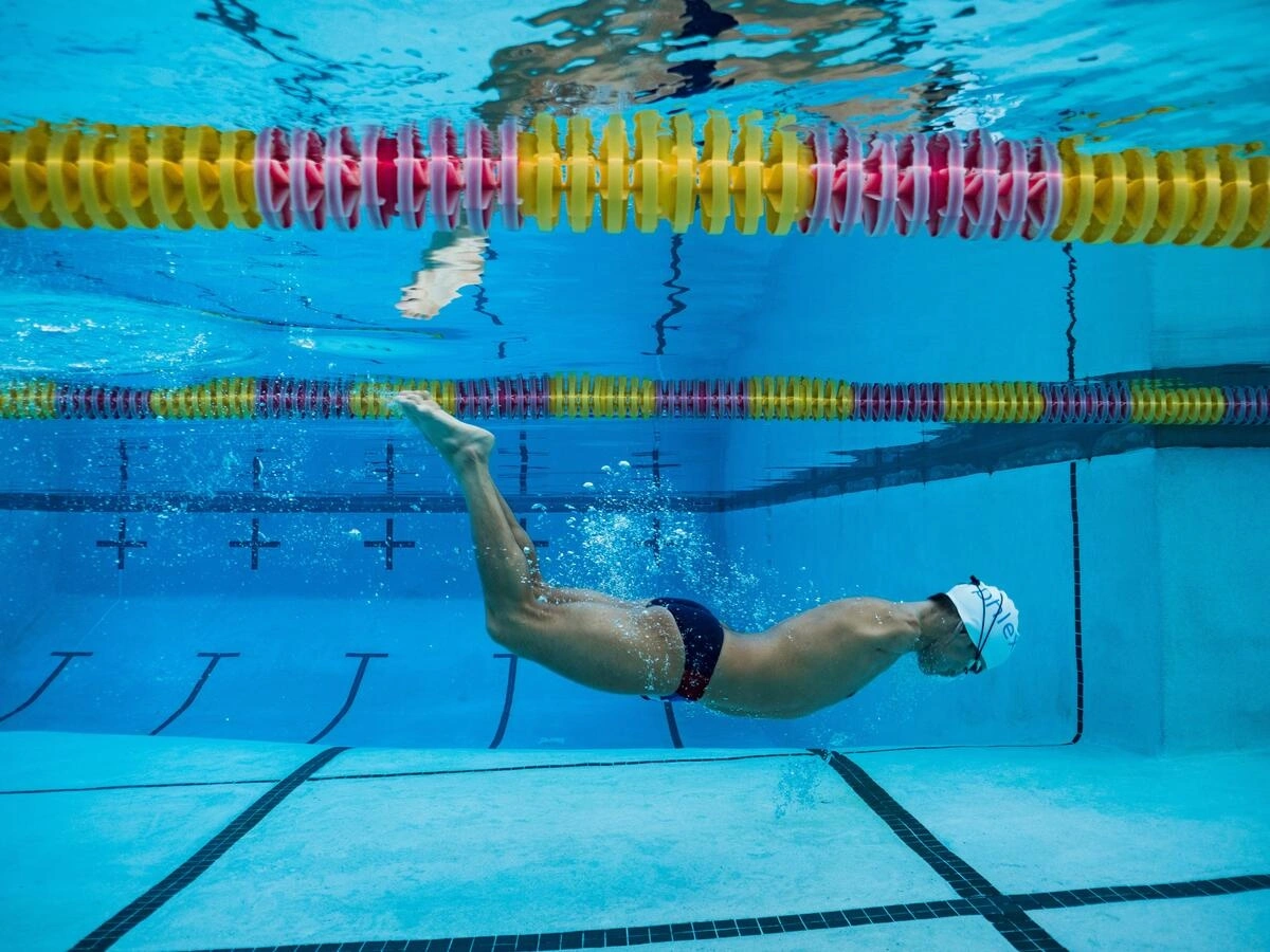 Une personne nage dans une grande piscine. Cette personne n'a pas de bras.