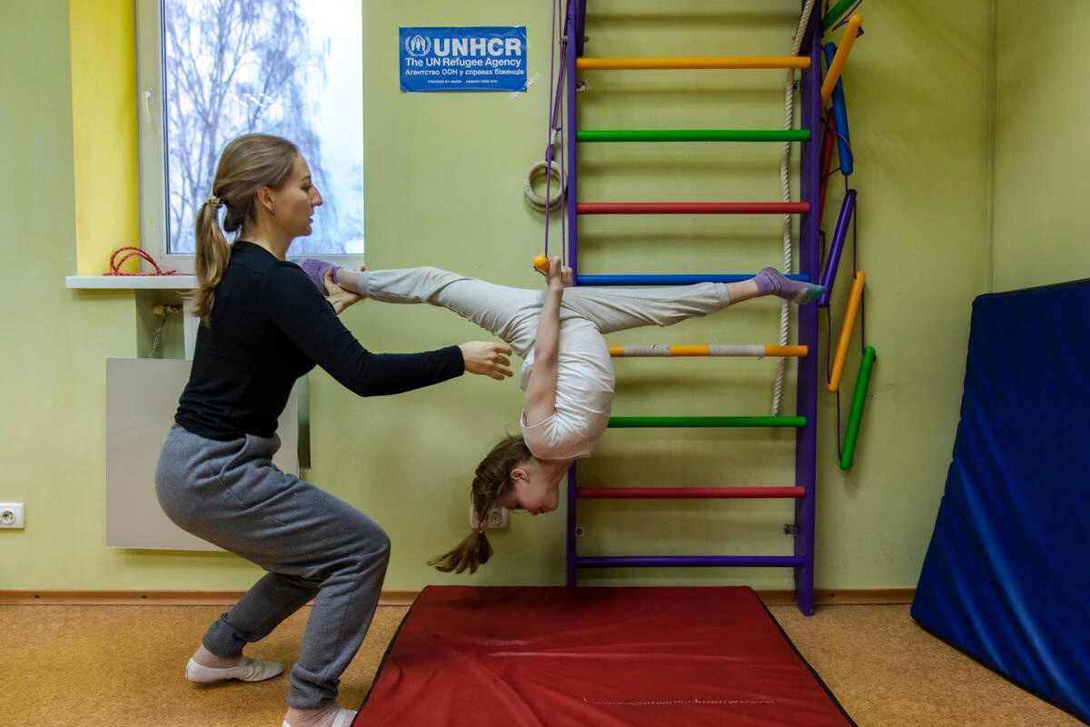 Une femme aide une jeune fille à s'étirer.