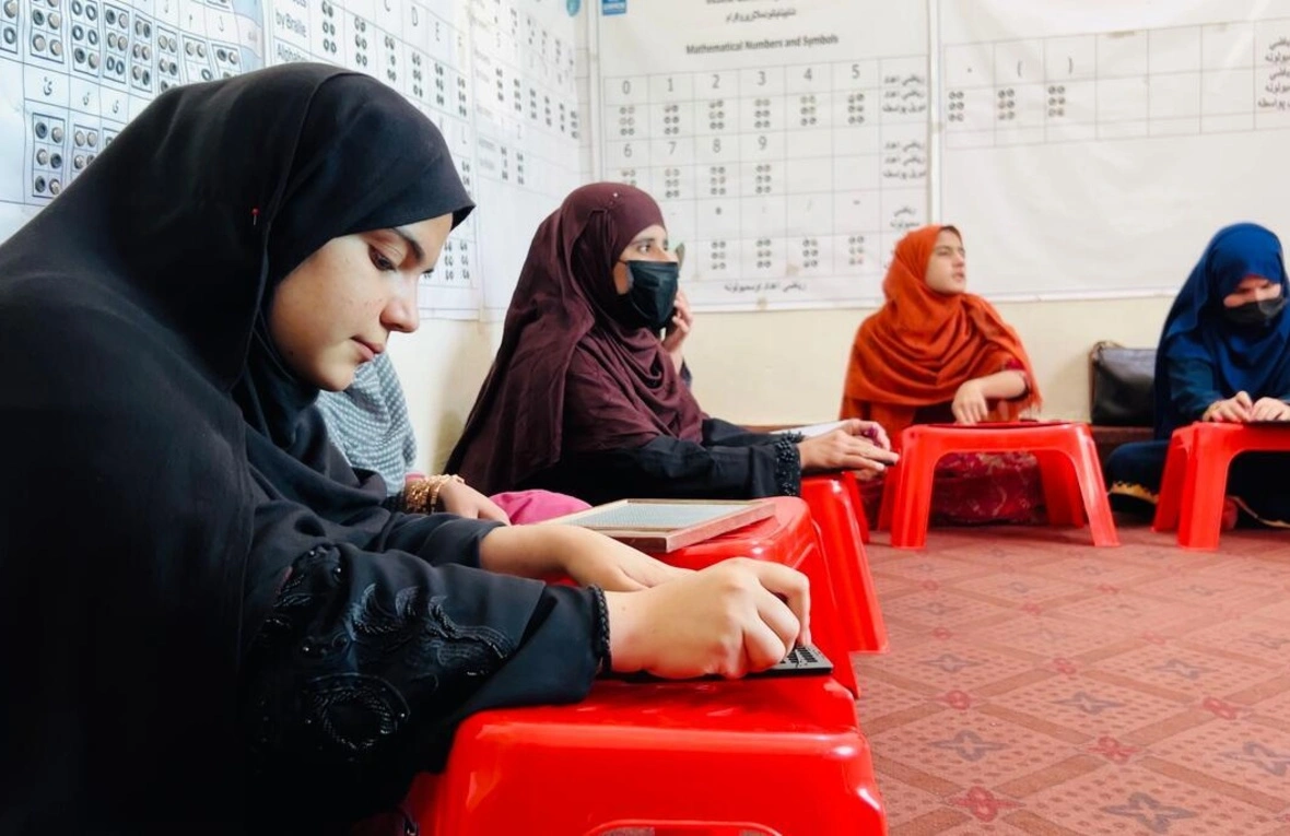 Un groupe de femmes assises sur le sol semblent être en train d'apprendre. Elles portent également toutes un foulard autour de la tête.