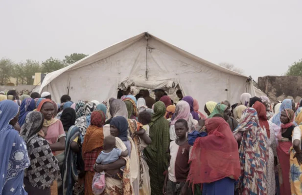 A large group of people are gathered in front of a big white tent.