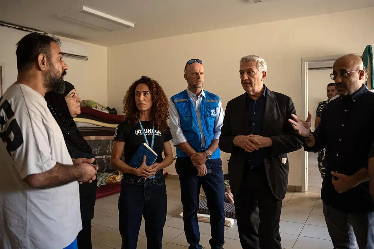 A group of six people, two women and four men, are standing in a room and talking. 
