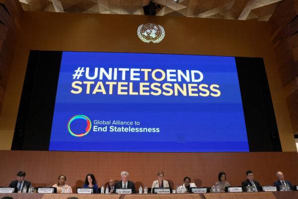 A screen above several people sitting at a desk facing the camera displays "#UNITEDTOENDSTATELESSNESS" alond with the Global Alliance to End Statelessness's logo.