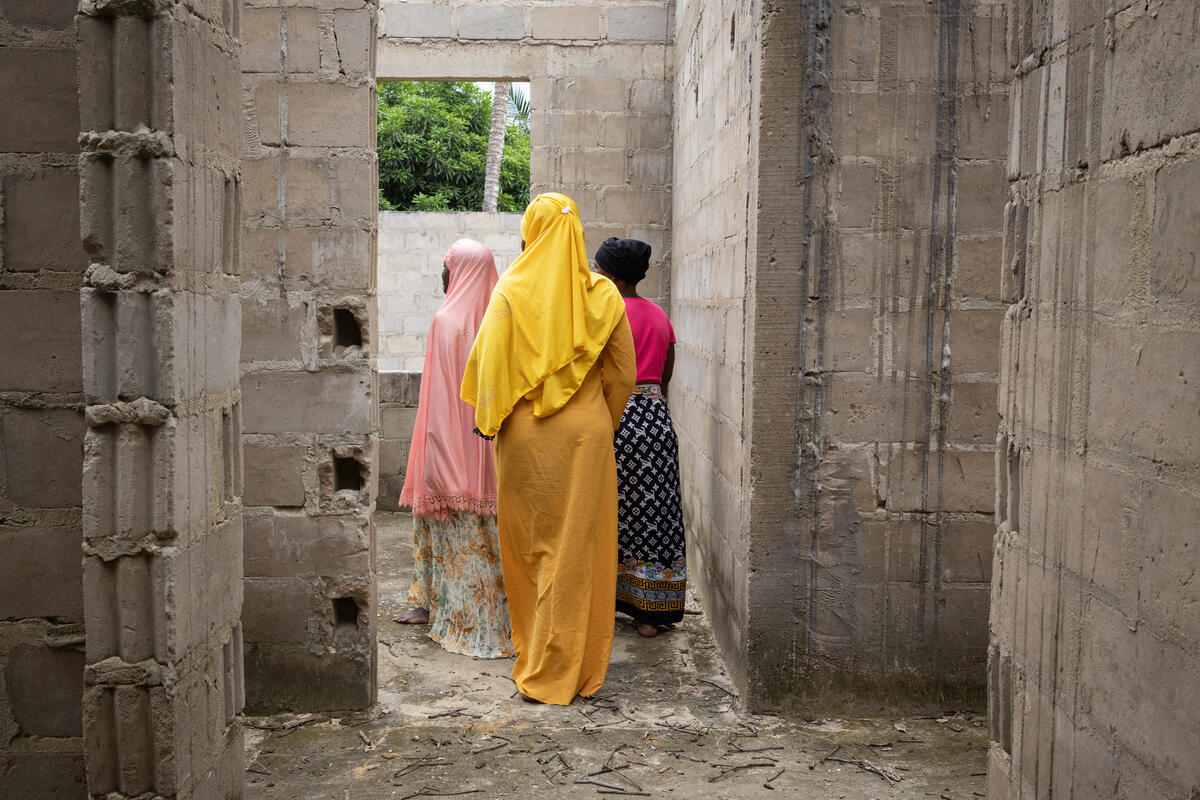 Trois femmes marchent à travers un bâtiment abandonné. Elles portent des tuniques colorées jaunes et roses.