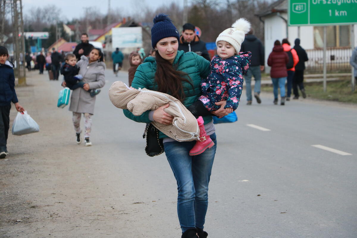 A woman is walking down the street carrying on her two children on each arm. 