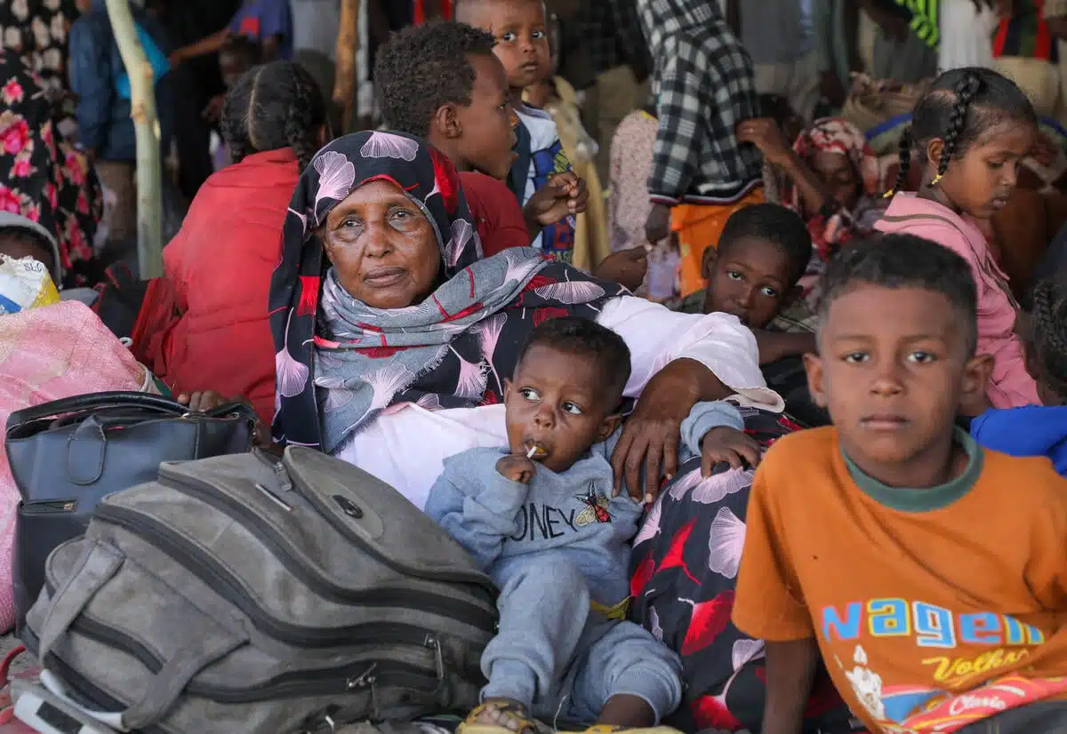 Une femme soudanaise et ses petits-enfants sont assis par terre au milieu de montagnes de bagages dans un centre d'accueil bondé au Sud-Soudan.