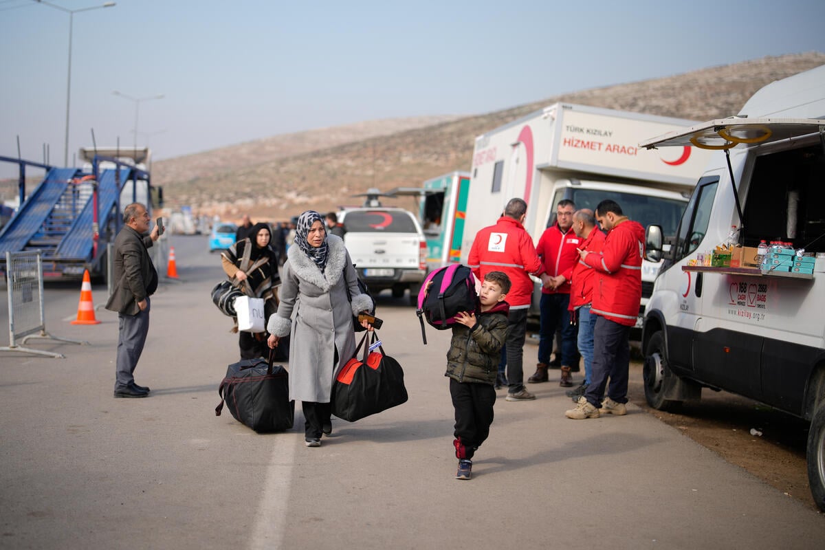 A woman and a child are carrying backpacks in the middle of the road. Both are wearing warm clothes in shades of grey and black.
