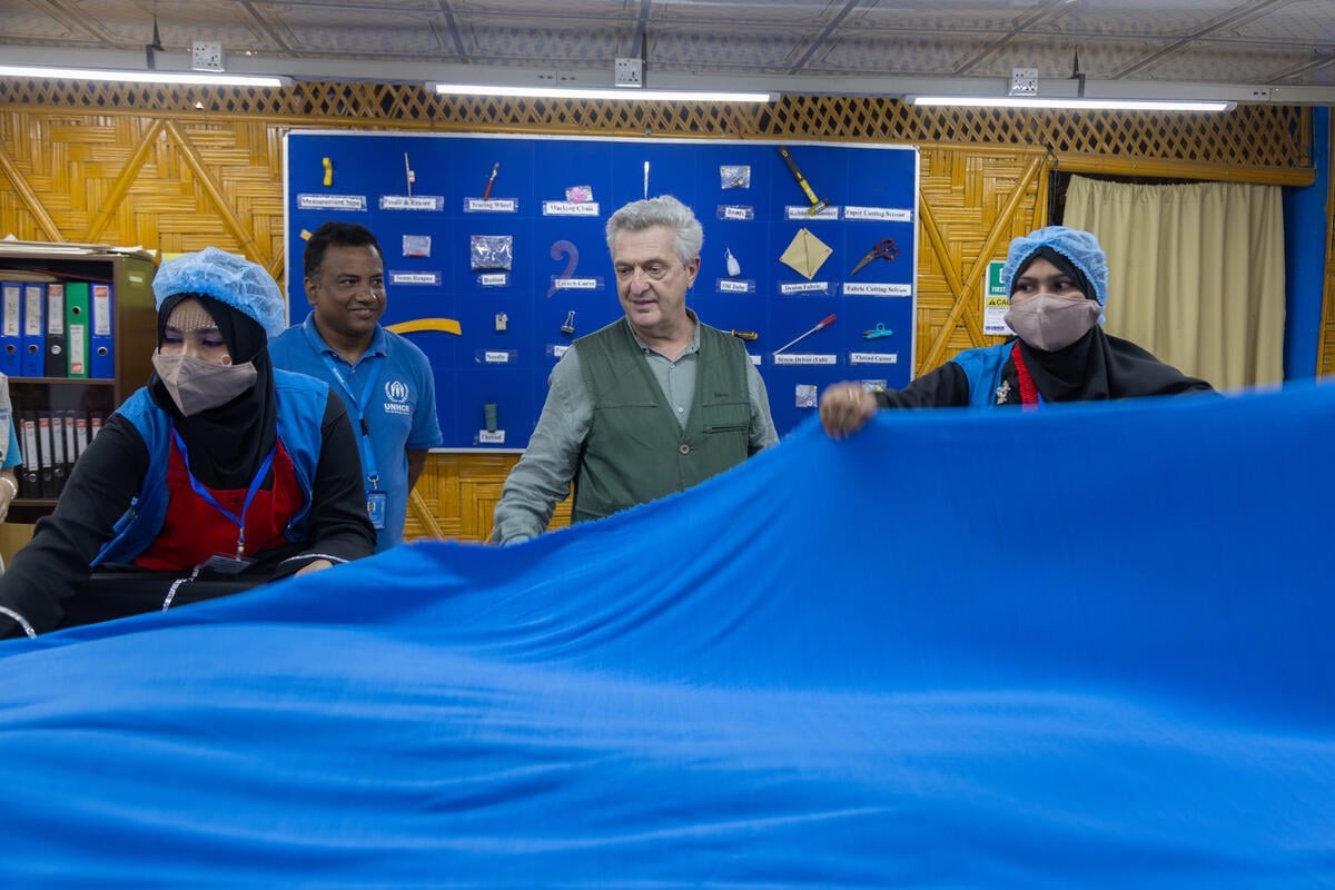 Le Haut Commissaire des Nations Unies pour les réfugiés, Filippo Grandi, se fait montrer un grand morceau de tissu bleu clair par deux ouvrières portant des résilles et des masques médicaux dans un centre de production. 