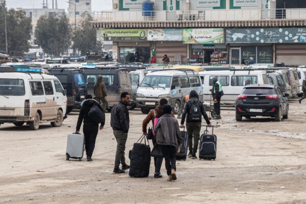 Syrian refugees returning from Türkiye carry their luggage across a parking lot filled with minivans and cars at the Bab Al-Hawa border crossing point in rural Idlib, Syria, in February 2025.