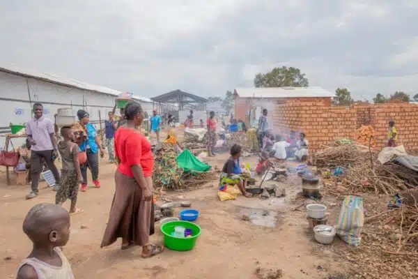 A group of Congolese refugees is seen cooking on fires and washing their dishes in plastic basins outdoors.