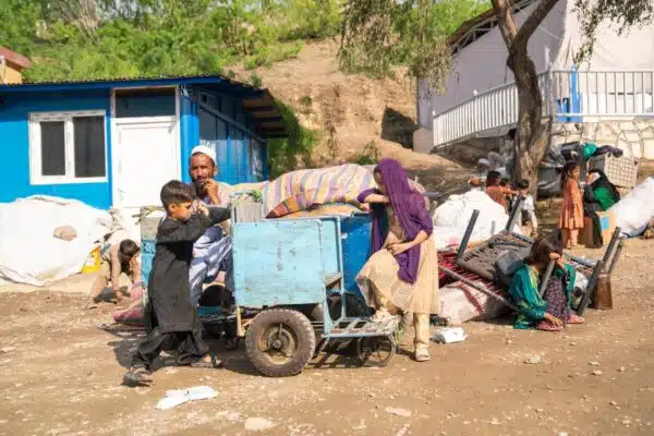 An Afghan man sits next to a pile of belongings as his children - a boy and a girl - are seen standing next to a small cart.