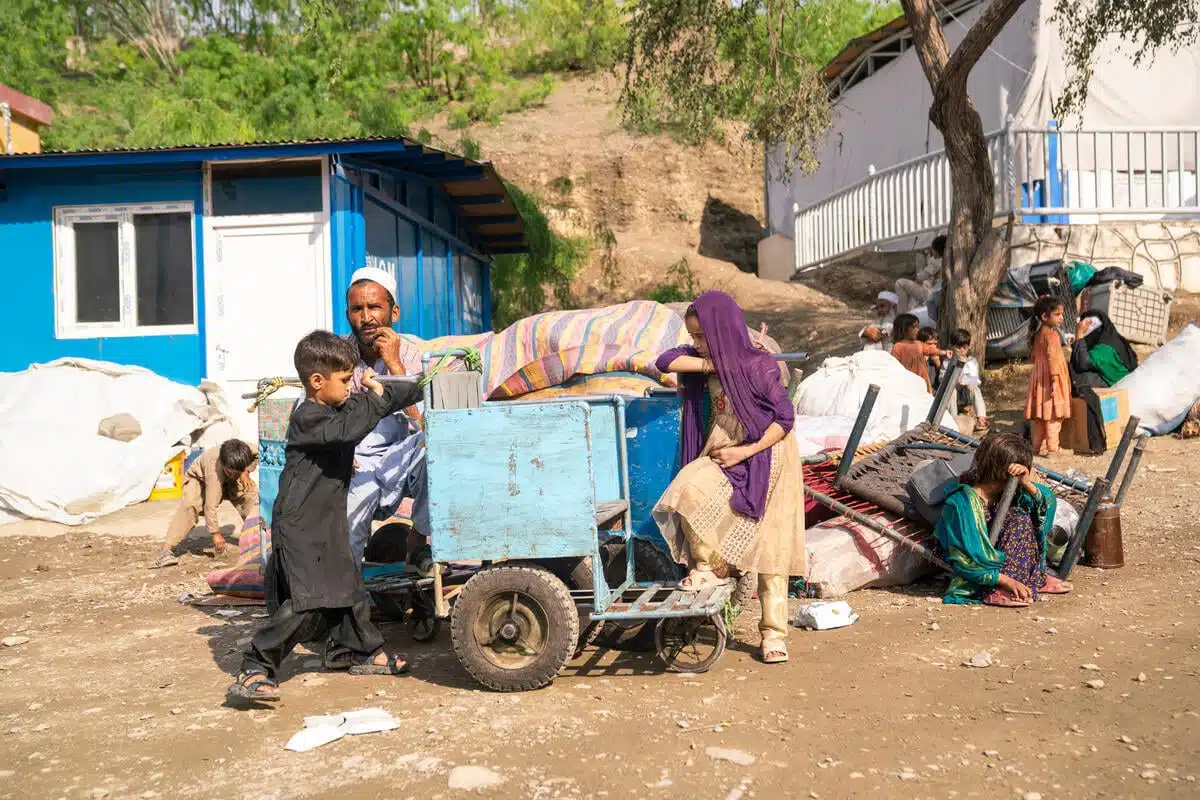 Un Afghan est assis à côté d'une pile de biens, tandis que ses enfants - un garçon et une fille - se tiennent à côté d'une petite charrette.