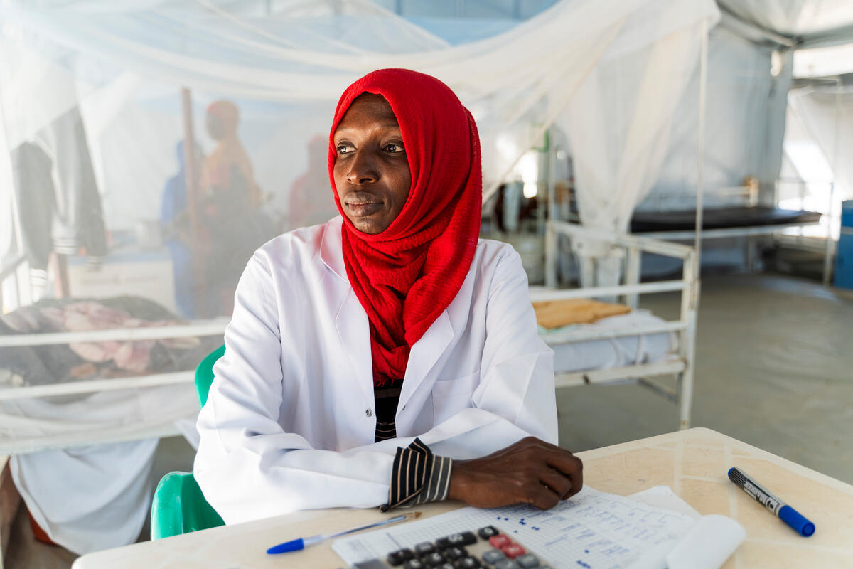 A woman doctor is seated, looking to her right. She appears thoughtful and calm, wearing a stunning red scarf on her head.