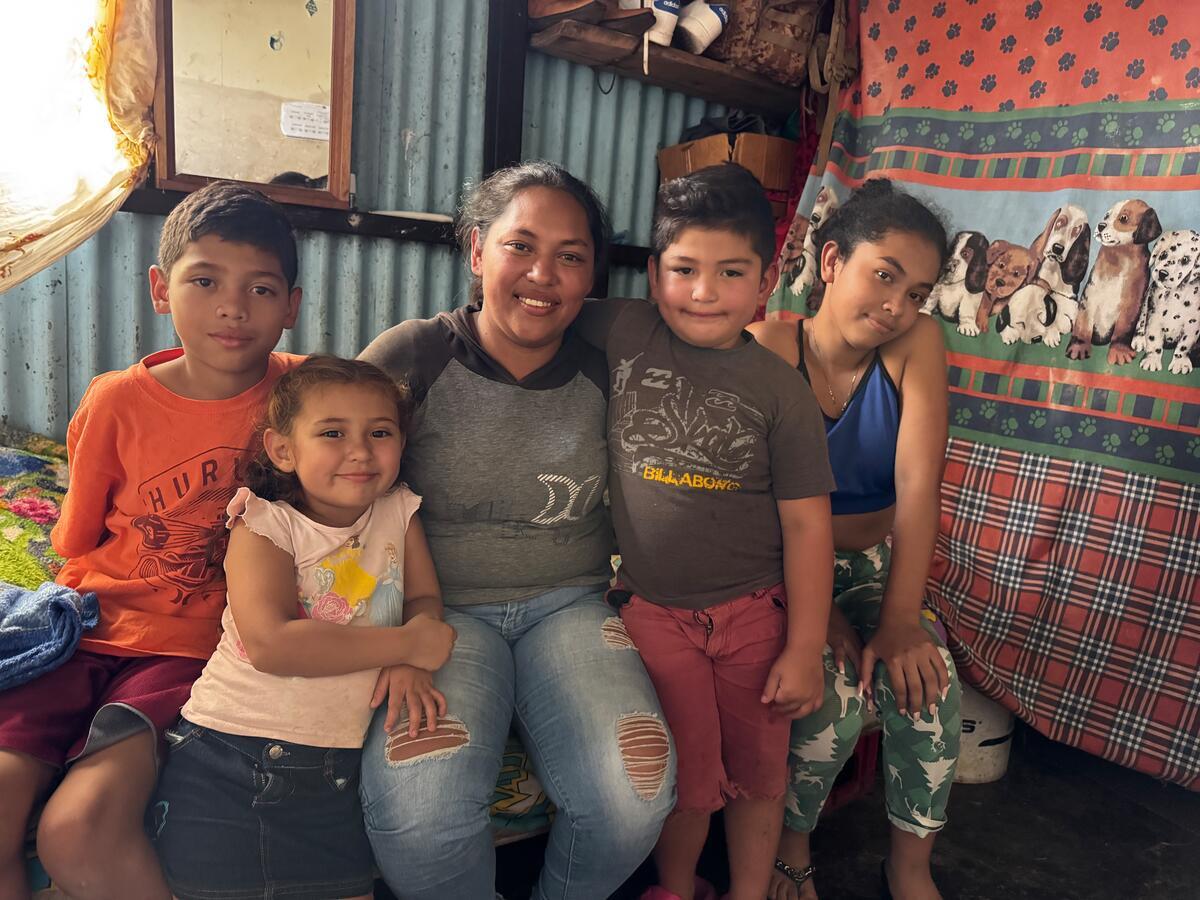 A family are seated together and hugging each other in a room while smiling at the camera.