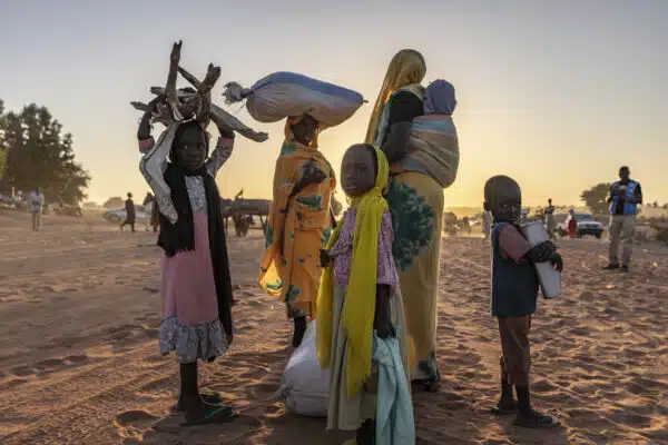 Un groupe de femmes et d’enfants soudanais est aperçu marchant dans le désert, dans le pays voisin du Tchad, alors que le soleil se couche derrière eux.