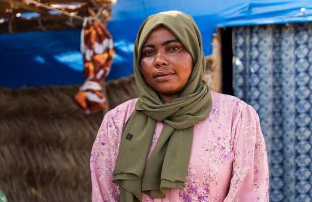 A woman wearing a green scarf on her head and a pink blouse looks thoughtful as she gazes at the camera.