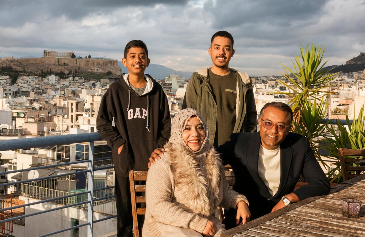 A family on a rooftop is posing happily for the camera. The man has his arm around the woman next to him, and two young boys are standing in the back, smiling.