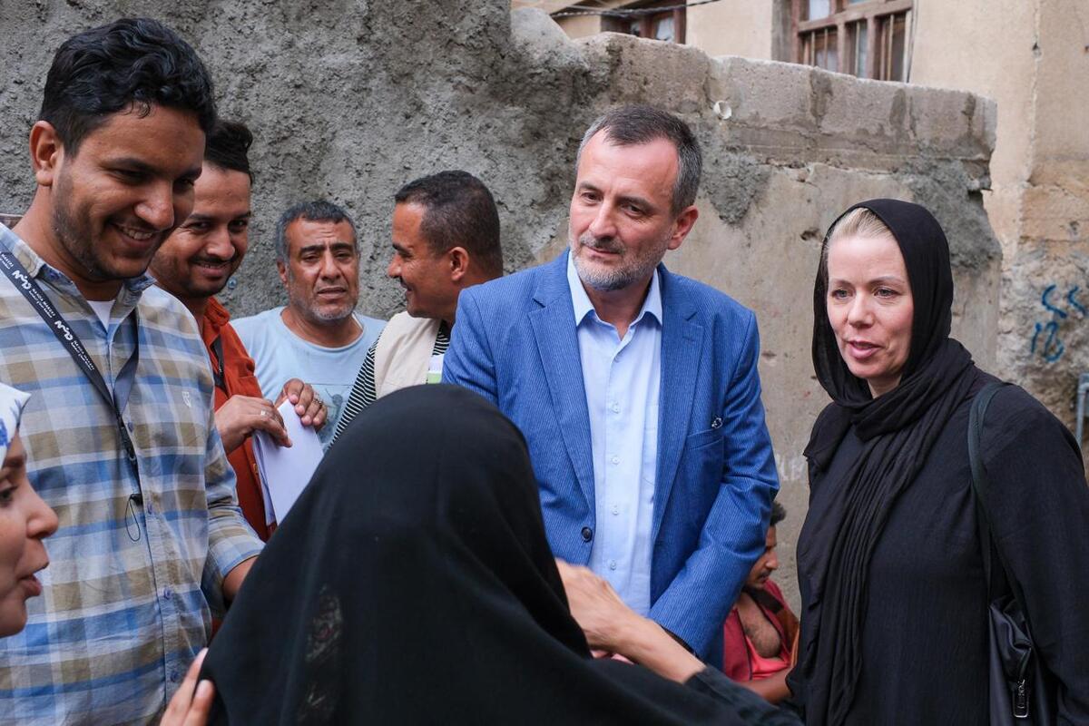 A man in a blue suit is talking to two women dressed in black, their heads covered by tunics.
