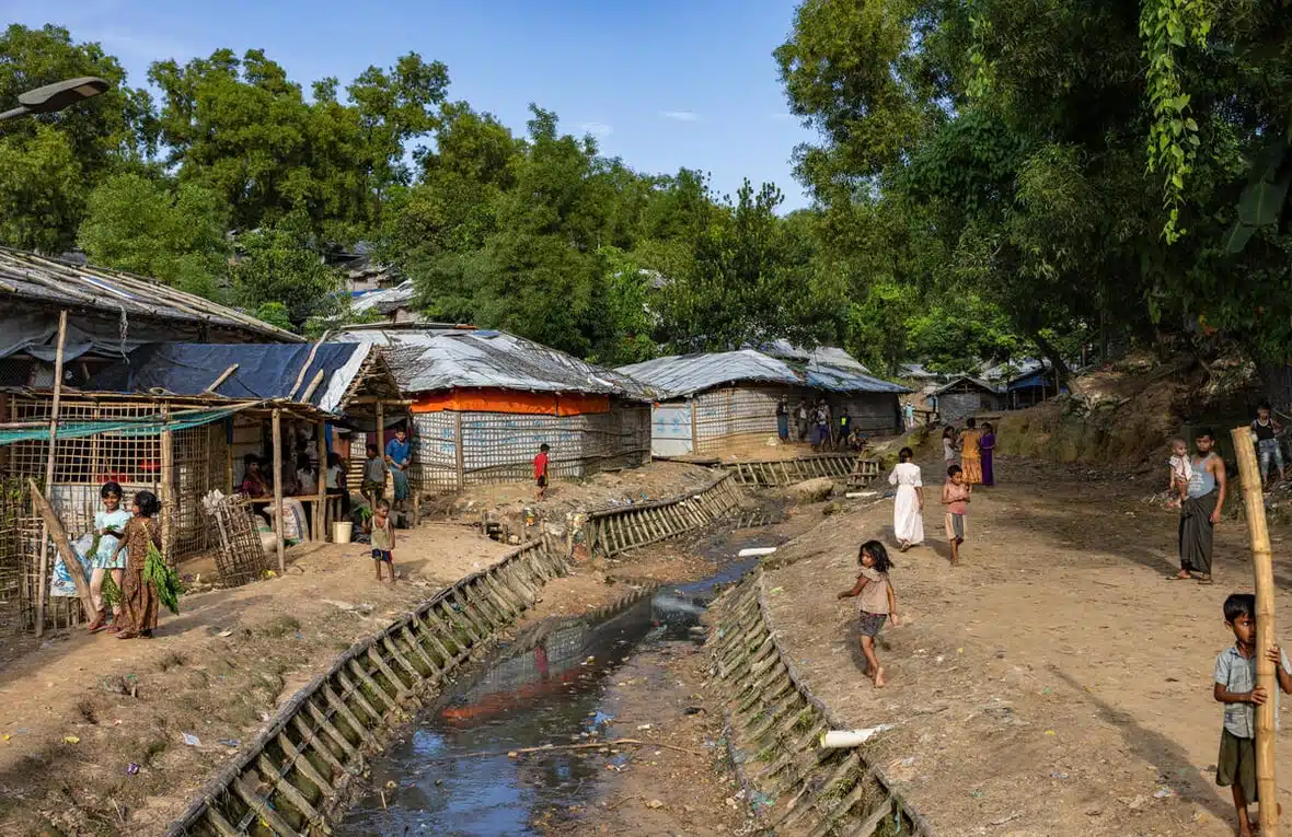 Des femmes et des enfants marchent le long d'un fossé profond renforcé sur les côtés par des poteaux en bambou et dans lequel s'écoulent des eaux usées.