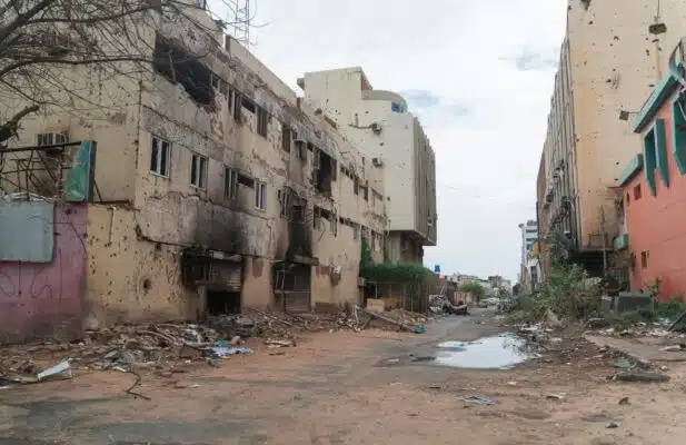An empty street with buildings bearing the marks of heavy fighting, including impacts from shells, bullet holes and fire damage is seen in the image.