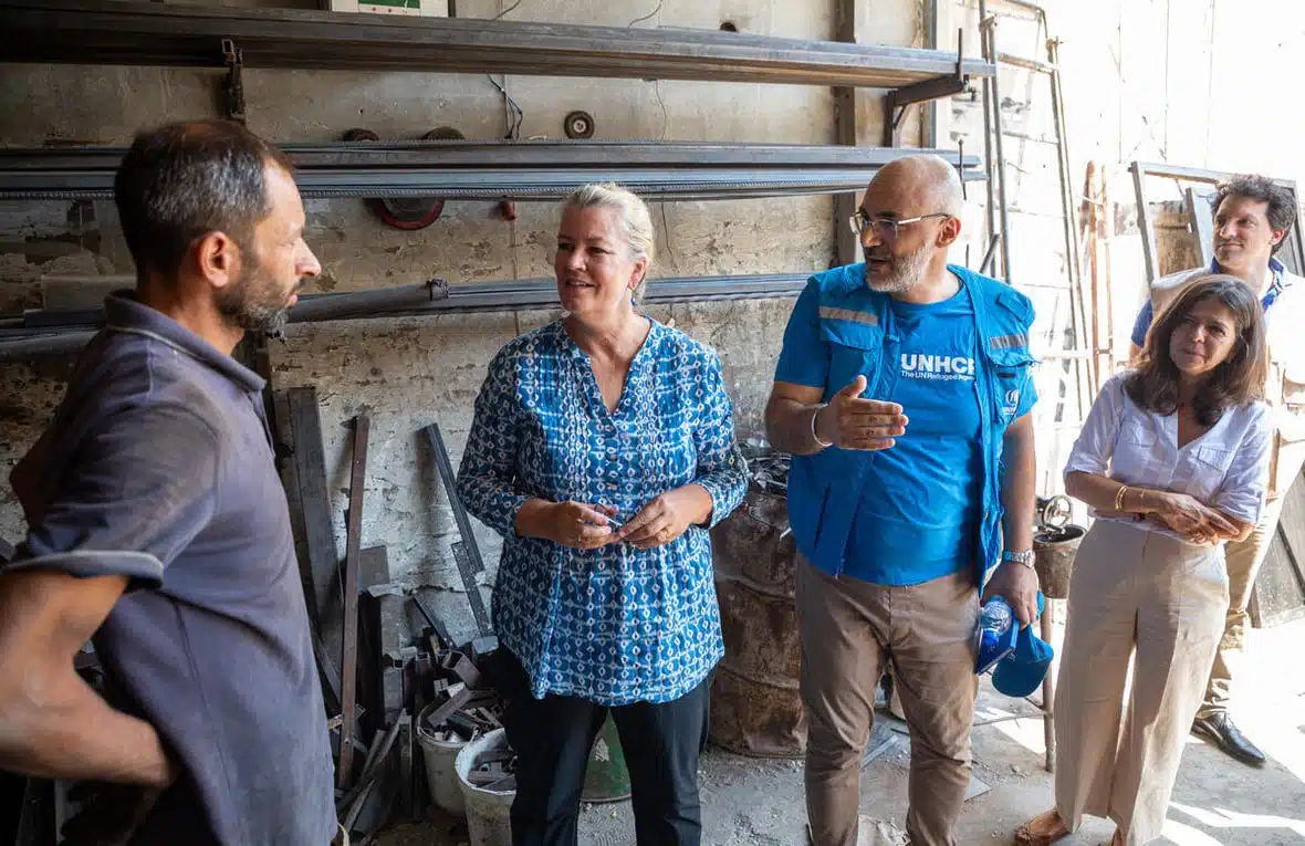 A middle-aged man speaks with Deputy High Commissioner Kelly T. Clements at a metal shop while three other people listen intently to their conversation.