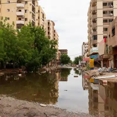 A street filled with water. Apartment buildings on the left and right, with green trees framing the left side of the frame.