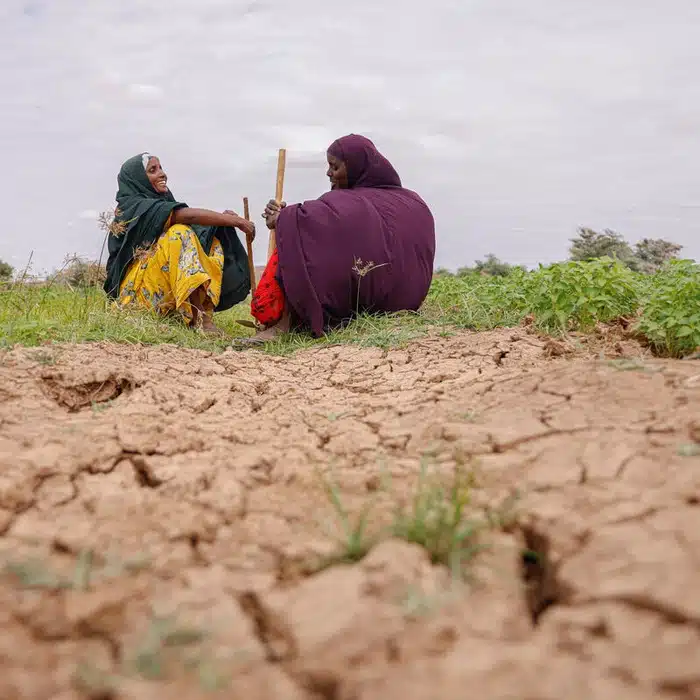 Two women sitting on grass surrounded by extremely dry earth.